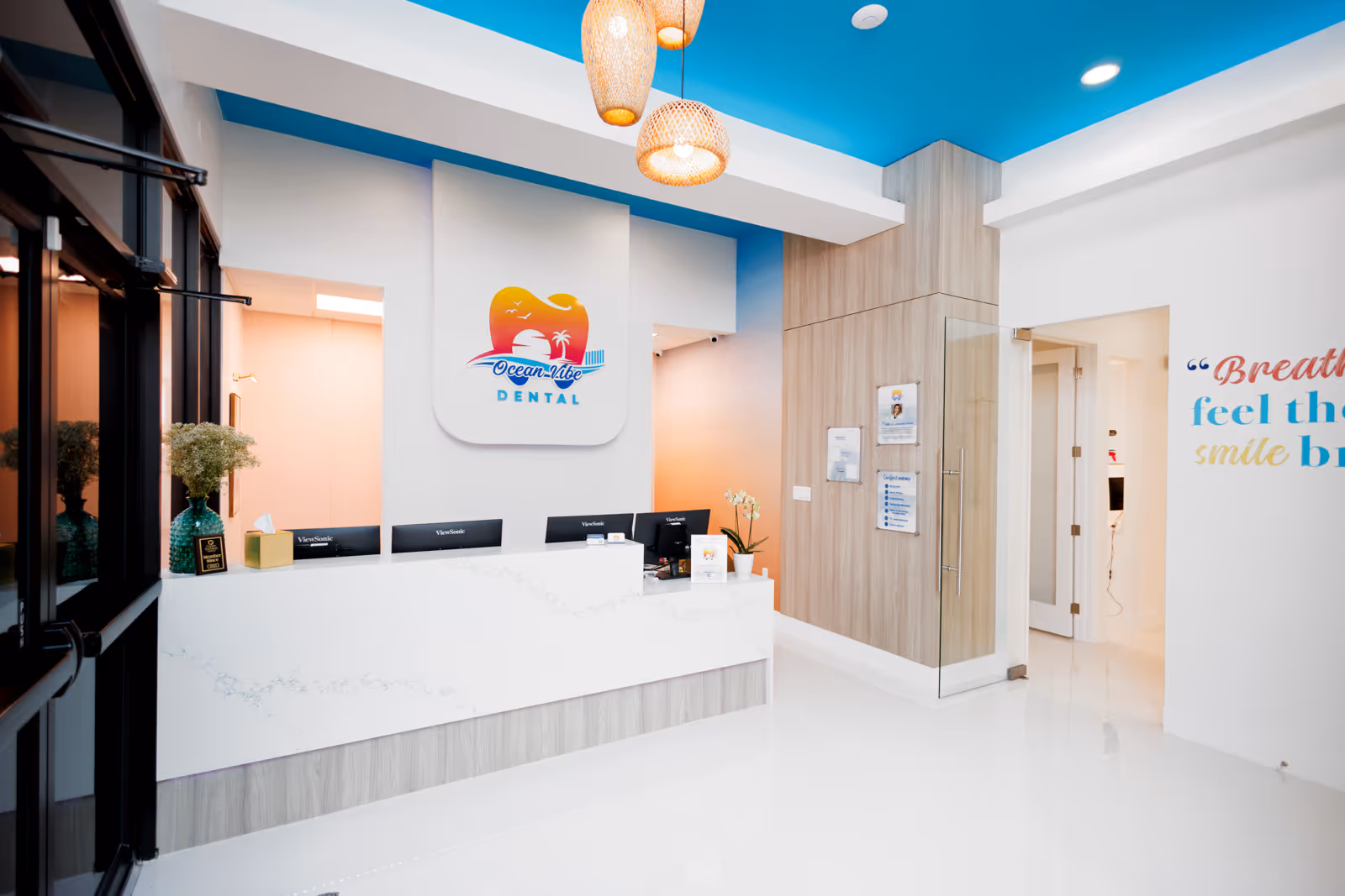 Bright modern dental office reception area with a white desk, blue ceiling, and Ocean Vibe Dental logo on the wall.