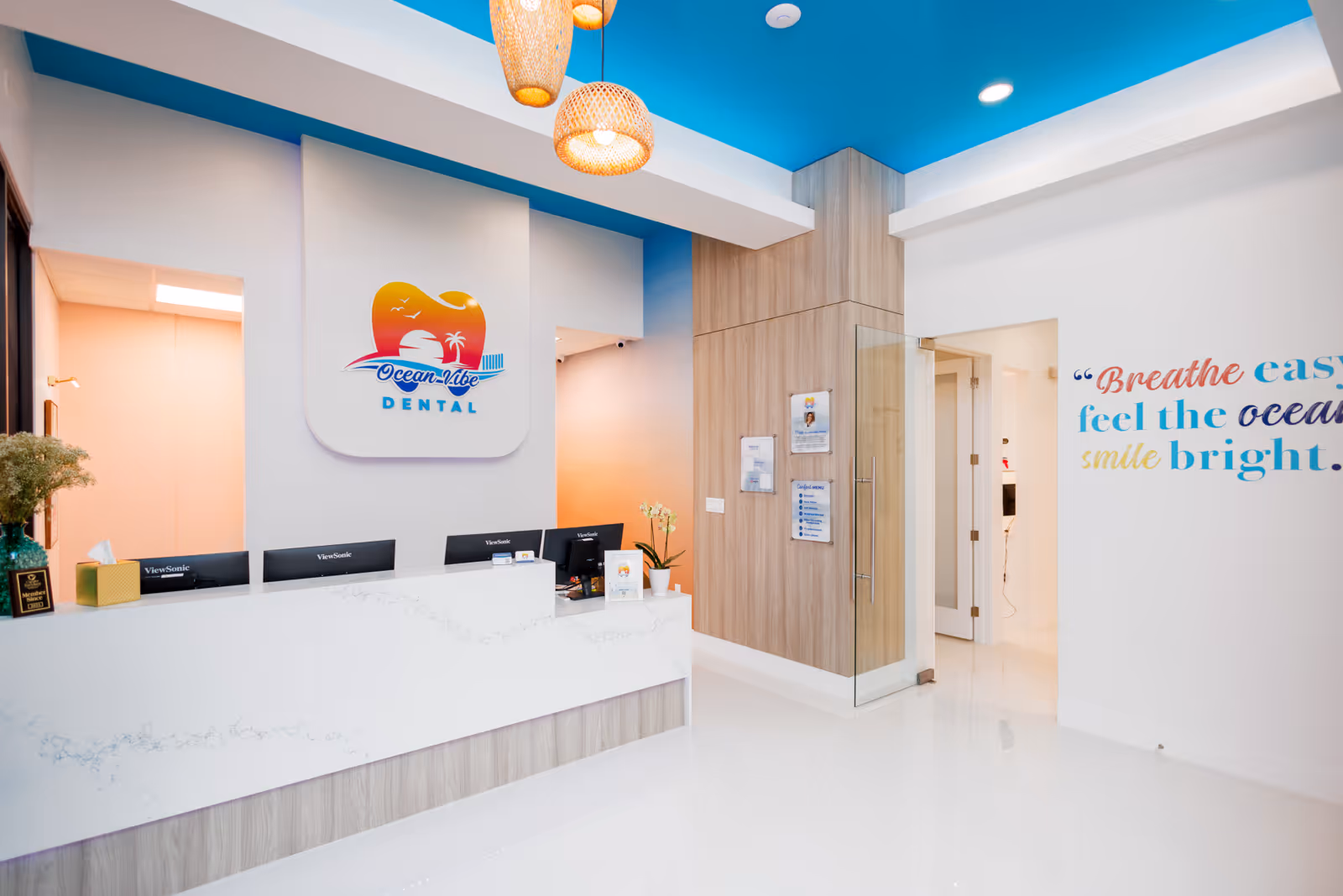 Modern dental office reception with white marble counter, blue ceiling, and Ocean Vibe Dental logo on the wall.
