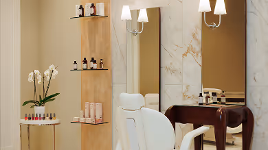 Heller Schönheitssalon mit weißen Stühlen, Regalen mit Kosmetikprodukten und großen Spiegeln an Marmorwänden.