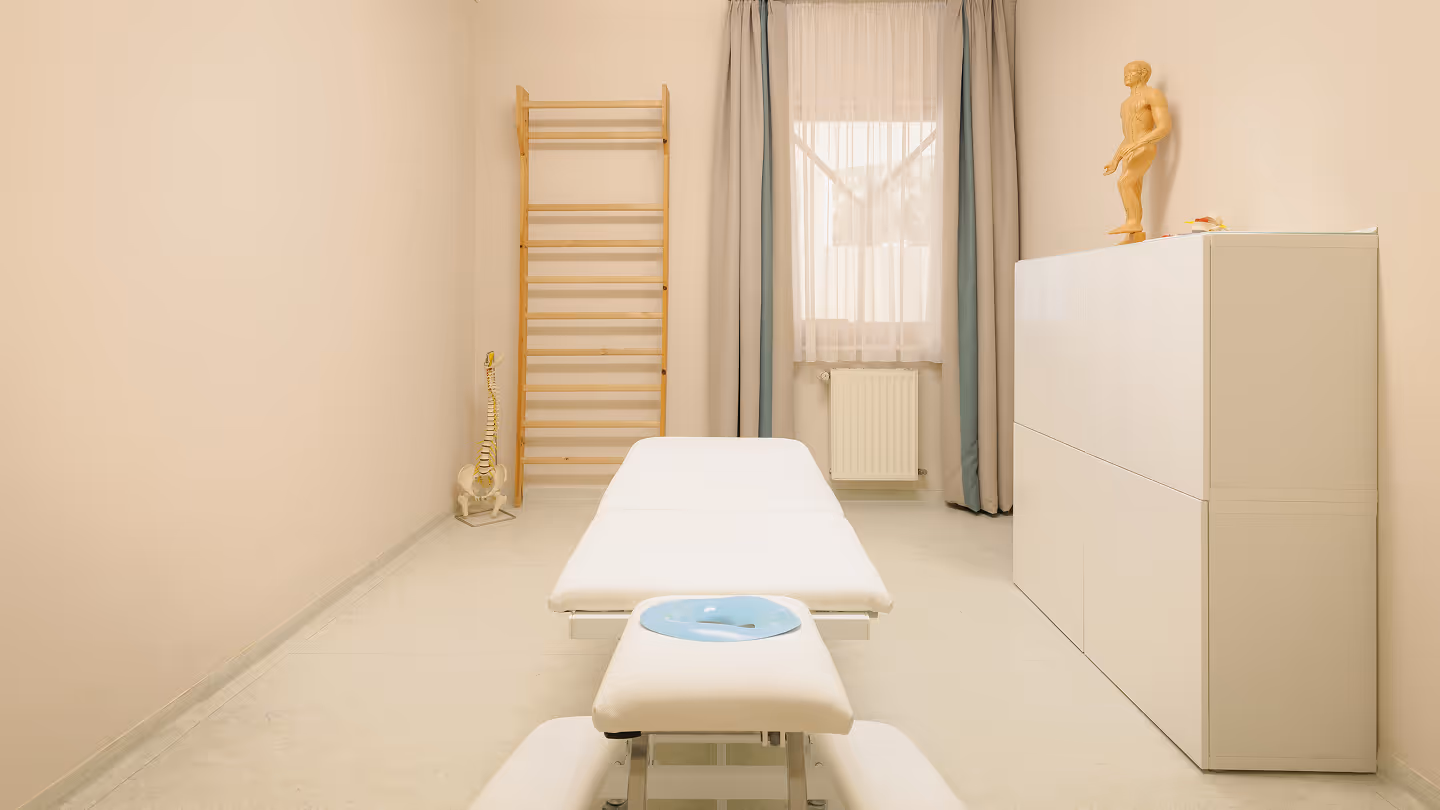 Helle Physiotherapiepraxis mit Behandlungsliege, anatomischem Modell der Wirbelsäule und Holzleiter an der Wand.