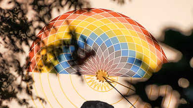 Bunte Windmühle oder Windrad mit gelben, roten und blauen Segmenten hinter Laub und Ästen im Gegenlicht.