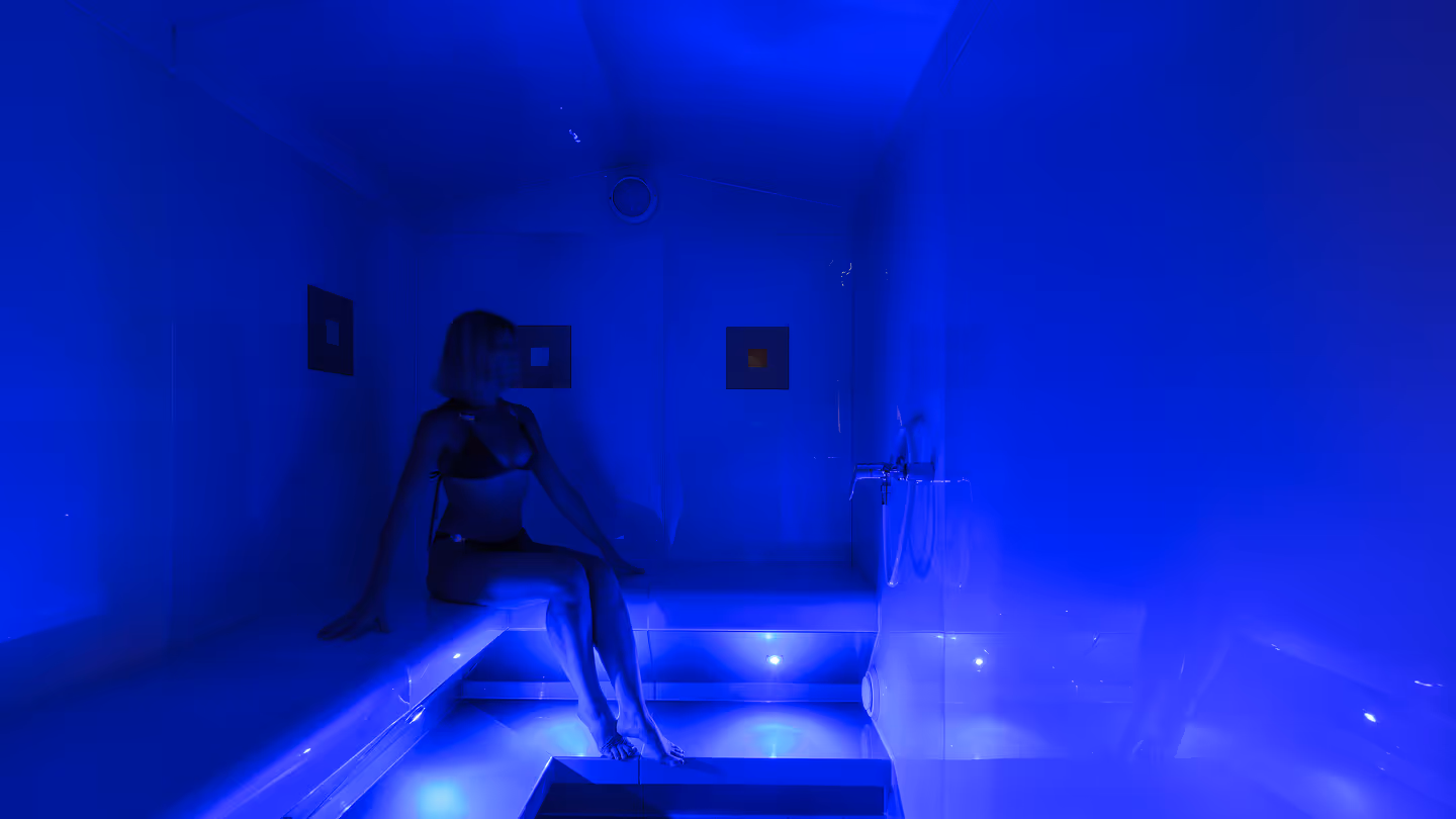 Frau in Bikini sitzt in einem blau beleuchteten Dampfbad oder Spa-Raum.