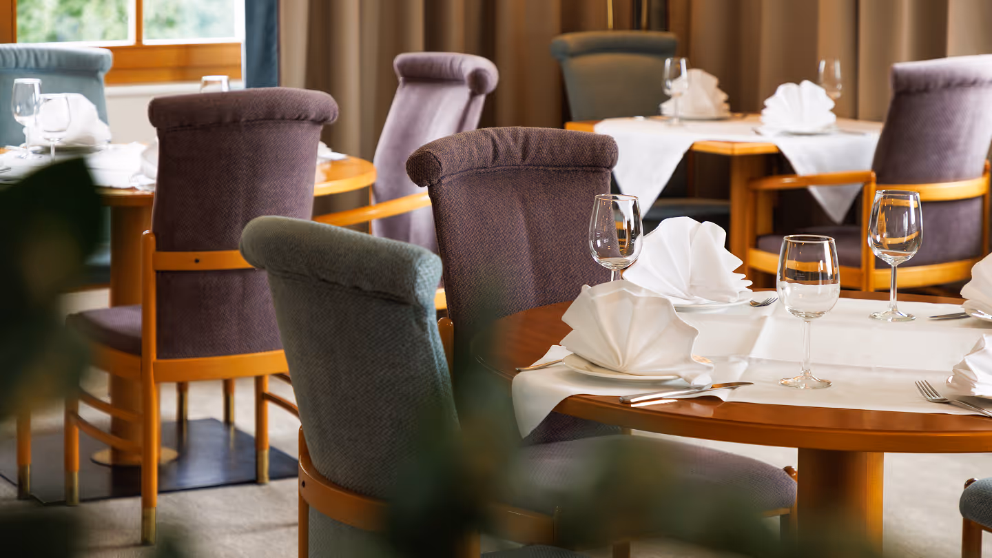 Elegantes Restaurant mit runden Holztischen, gedeckt mit weißen Servietten und Weingläsern, umgeben von gepolsterten Stühlen.