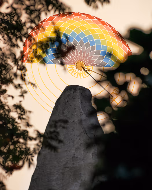 Heißluftballon mit buntem Muster hinter Baumzweigen vor hellem Himmel.