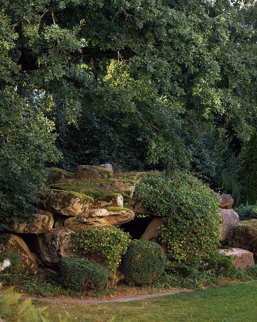 Ein natürlicher Steinhügel mit Moos bedeckt und von grünen Büschen und Bäumen umgeben.