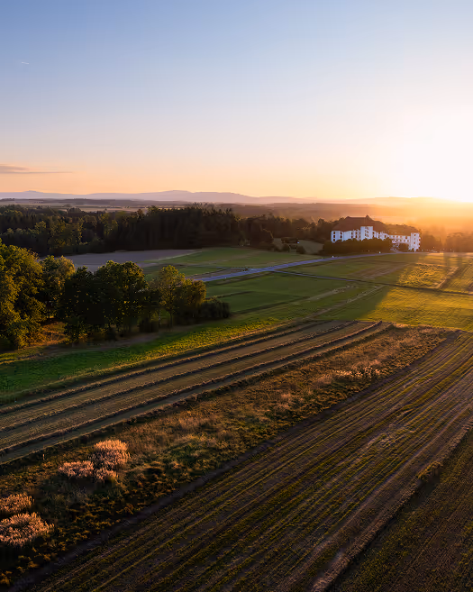 Landschaft mit landwirtschaftlichen Feldern und einem weißen Gebäude bei Sonnenuntergang.
