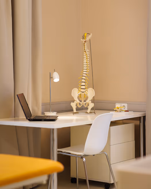 Moderner Schreibtisch mit Laptop, Lampe und einem Modell der menschlichen Wirbelsäule in einem Büro oder medizinischen Raum.