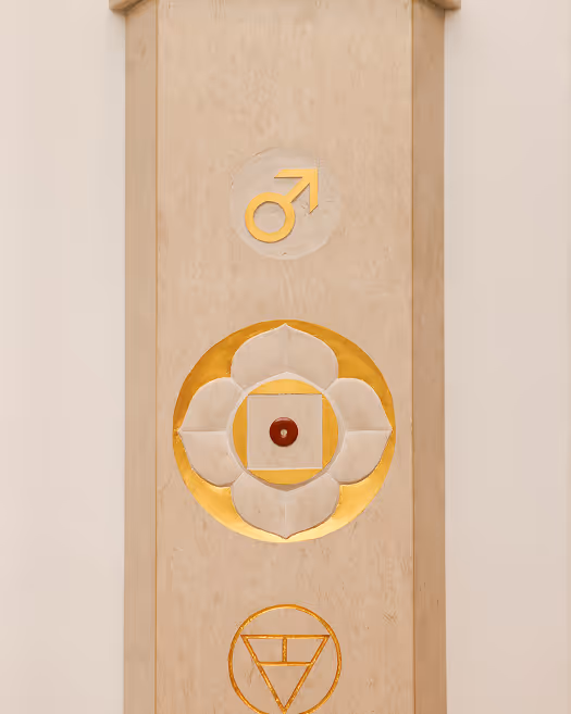 Holztafel mit goldfarbenen Symbolen, darunter männliches Geschlechtssymbol und florales Muster.