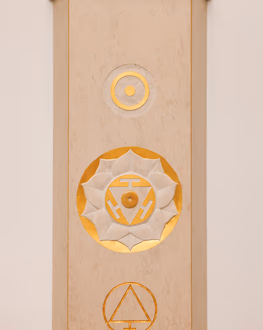 Drei goldene, runde Symbole mit spirituellen und geometrischen Mustern auf hellem Holz.