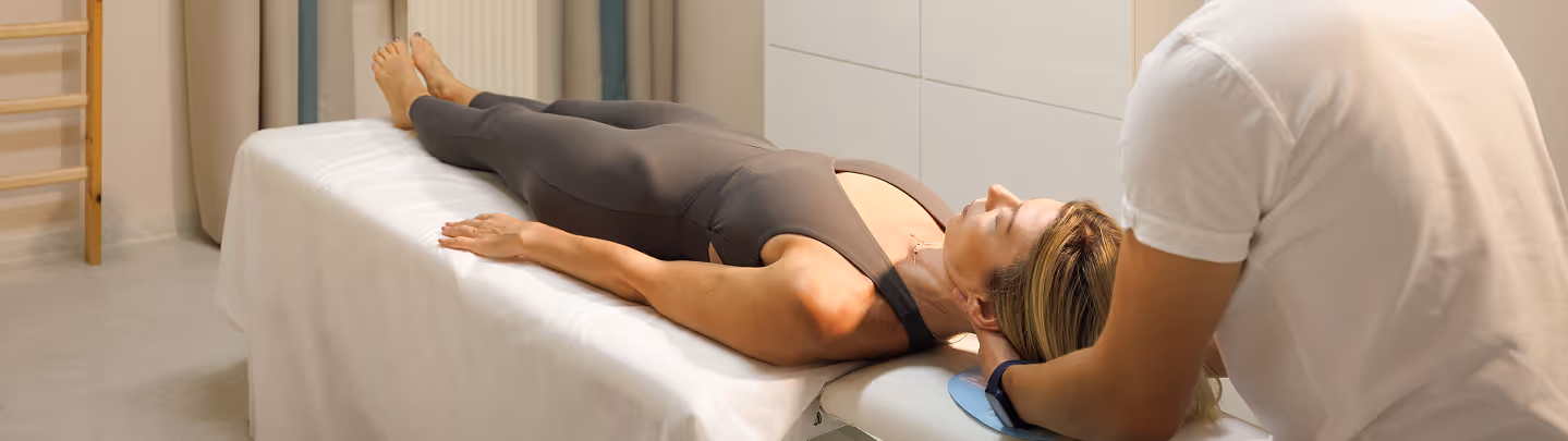 Frau liegt entspannt auf einer Behandlungsliege, während eine zweite Person ihren Nacken stützt.