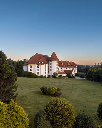 Großes weißes Schloss mit roten Dächern auf einem gepflegten grünen Rasen unter klarem Himmel bei Sonnenaufgang.
