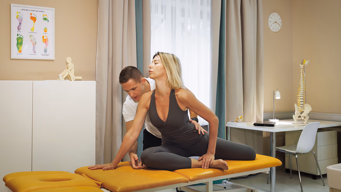 A physical therapist helps a woman do a stretching exercise on a treatment couch in a practice.