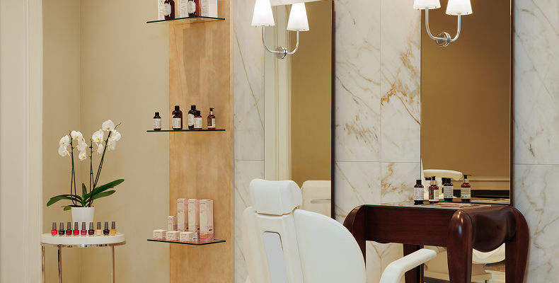 Eleganter Beauty-Salon mit weißem Behandlungsstuhl, Holztisch, Spiegeln, Orchideenblume und Kosmetikprodukten auf Regalen.