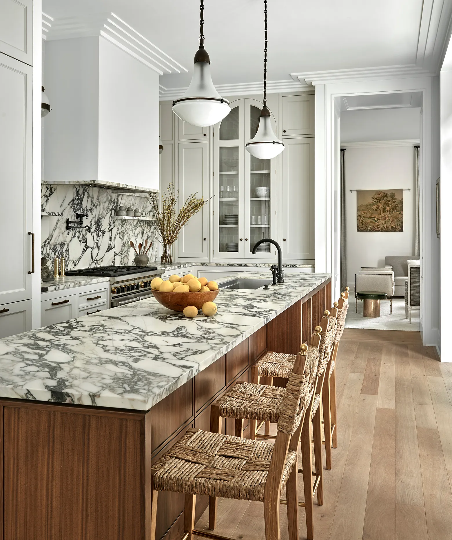 Modern kitchen with marble countertops, wooden island, woven chairs, and pendant lighting.