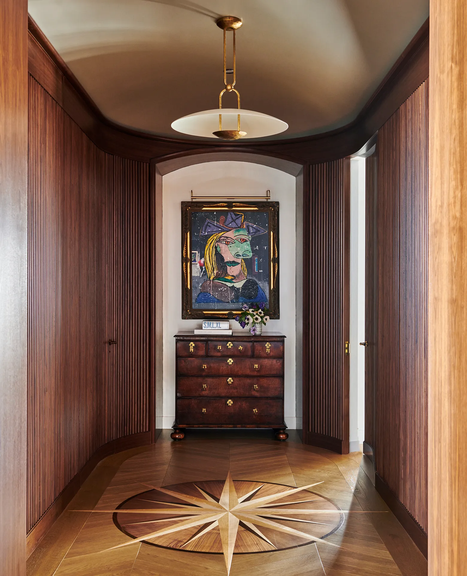 Hallway with wooden paneling, a compass rose floor design, a chest with flowers, and abstract portrait art.