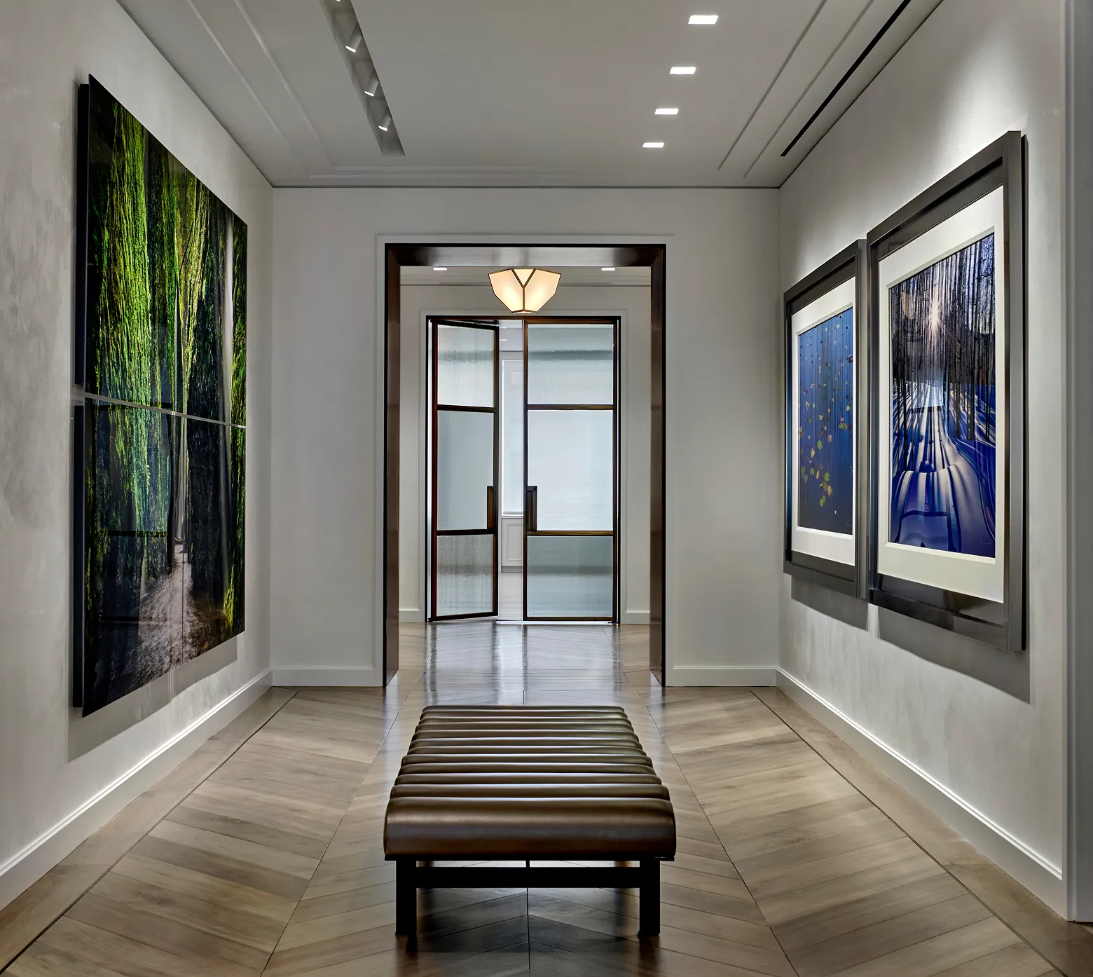 Gallery hallway with forest-themed artwork on walls and a brown bench in the center on wood flooring.
