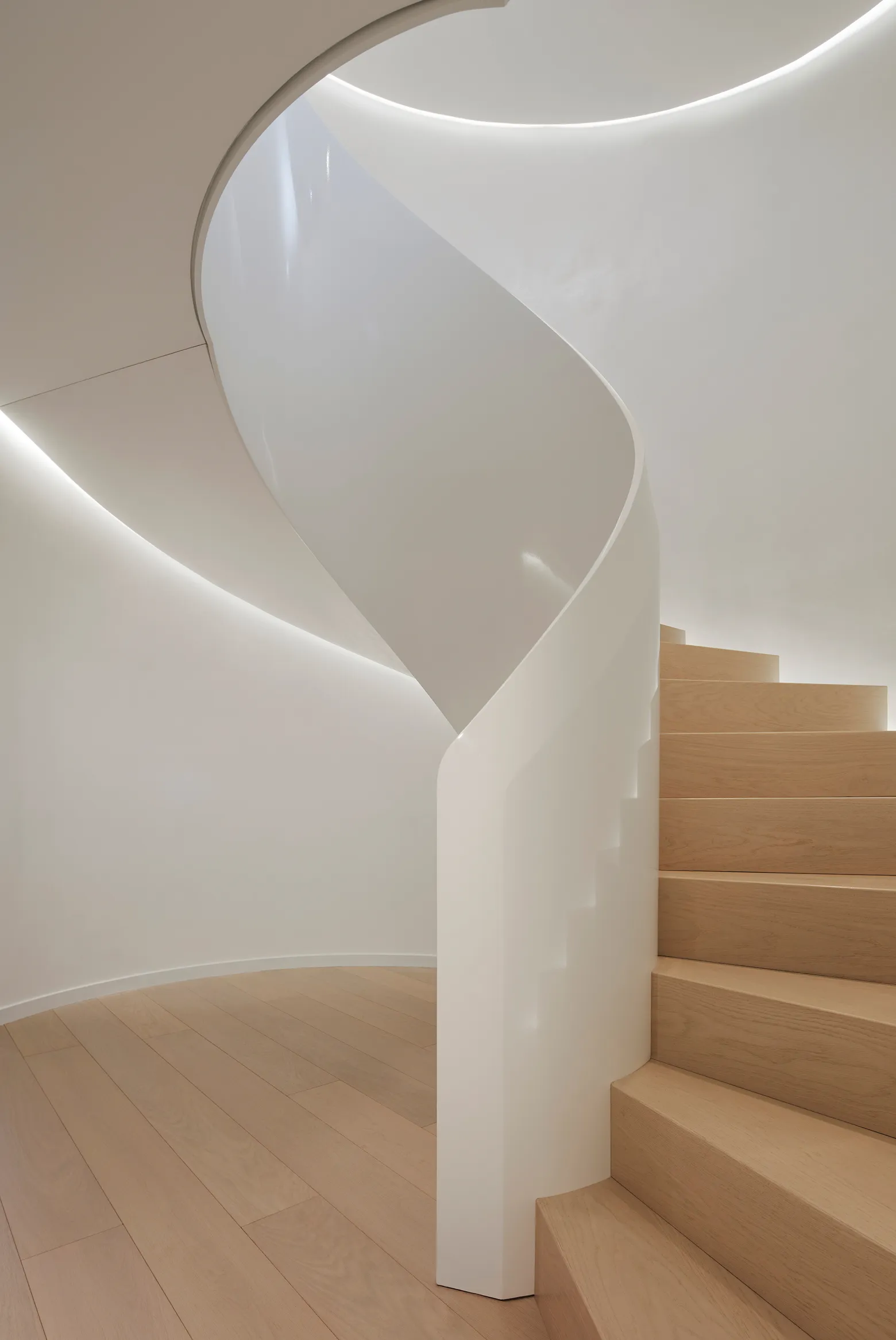Minimalist curved wooden staircase with smooth white banister and soft indirect lighting.