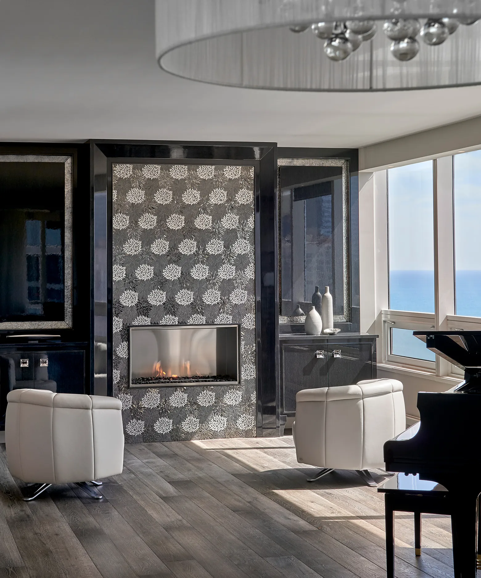 Modern living room with patterned fireplace, two white leather armchairs, ocean view, and black grand piano.