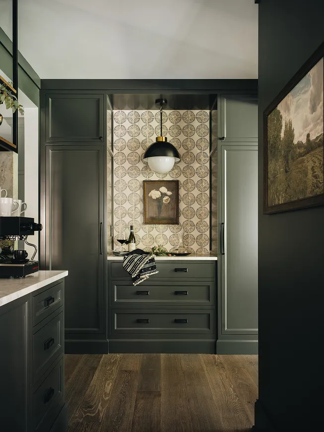 Dark green kitchen cabinetry with patterned tile backsplash and a hanging black and white pendant light.