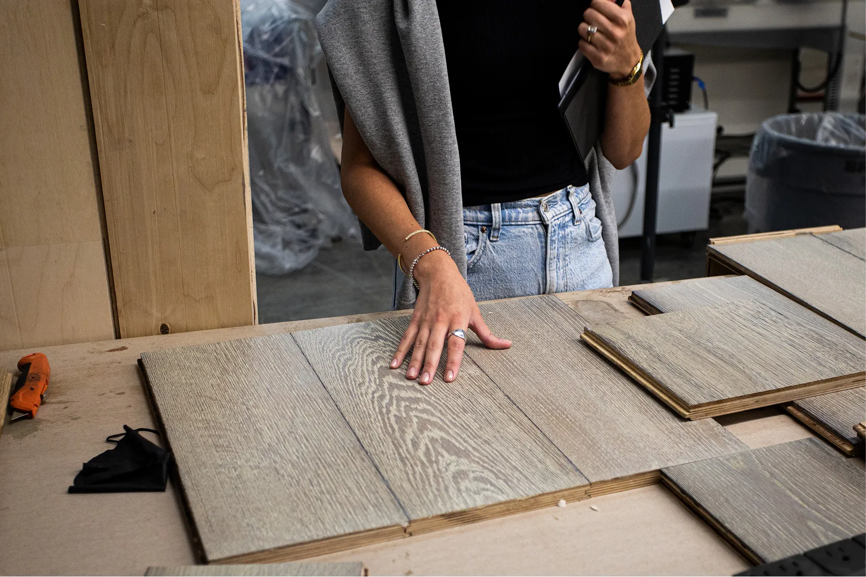 Person touching wood flooring samples laid out on a table in a workshop setting.