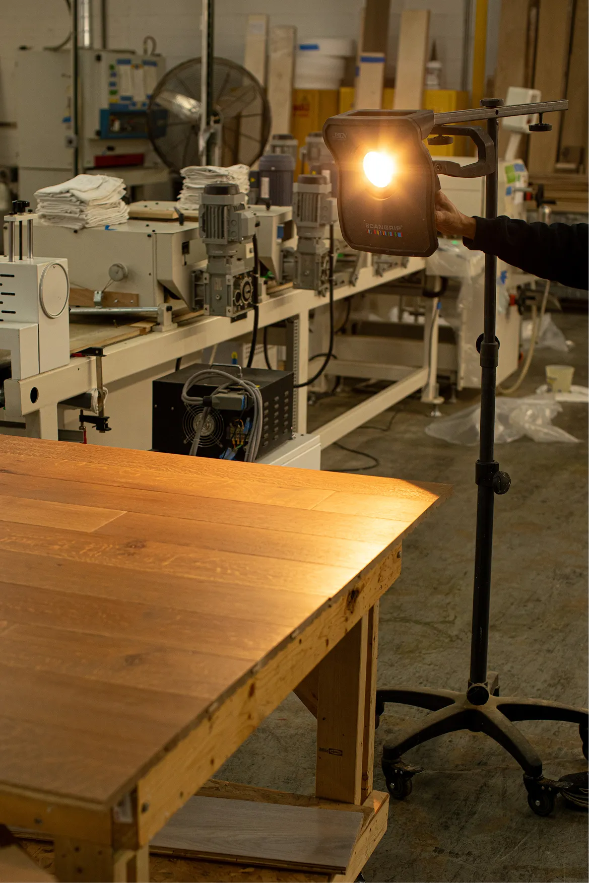 Workshop spotlight on wooden table with industrial machinery and fan in background.
