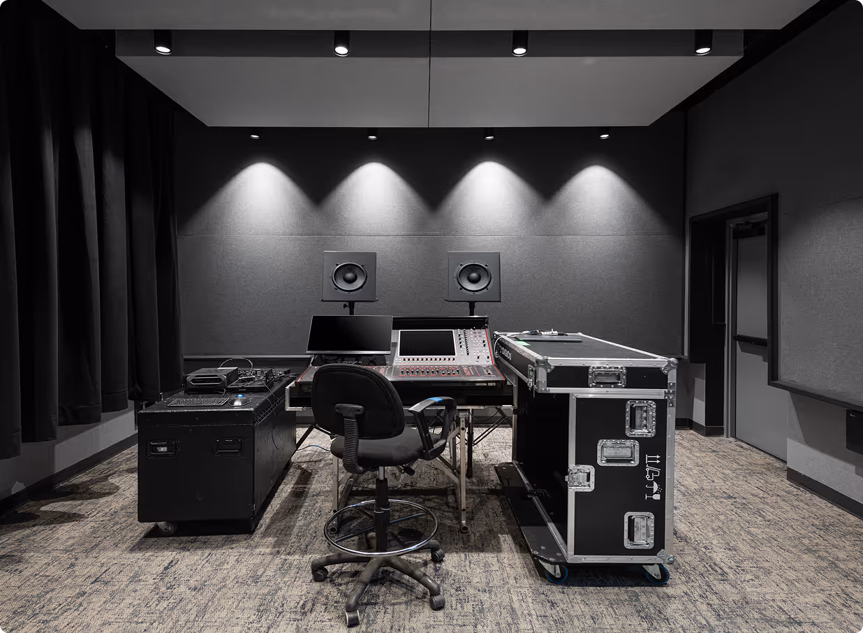 Modern audio mixing room with speakers, mixing console, computer monitors, and a black swivel chair on a carpeted floor.