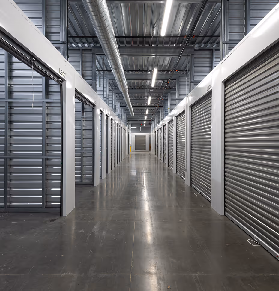 Interior view of a modern storage facility corridor with closed metallic roll-up doors and polished concrete floor.