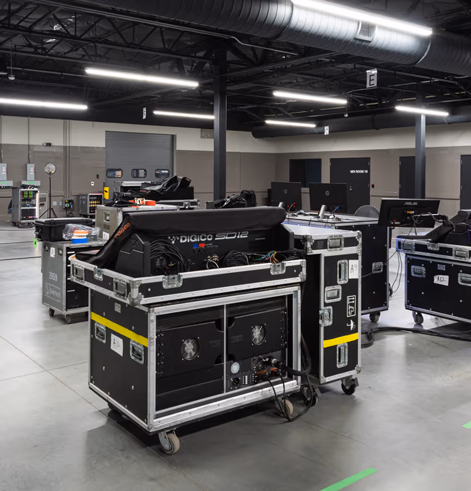 Industrial room with audio-visual equipment in black flight cases on wheels and workstations with computer monitors.