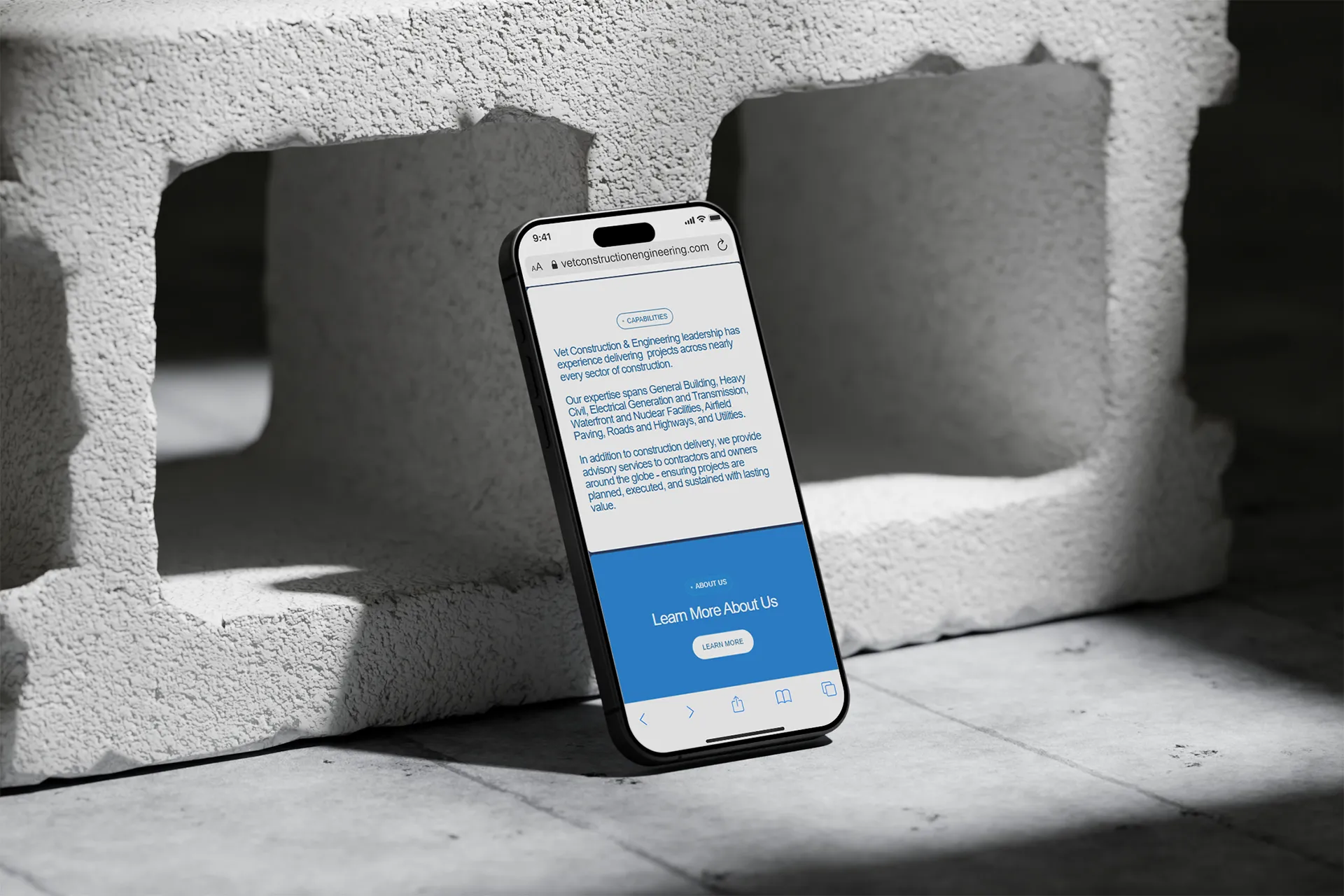 Smartphone displaying Vet Construction & Engineering website next to a concrete cinder block on a tiled floor.