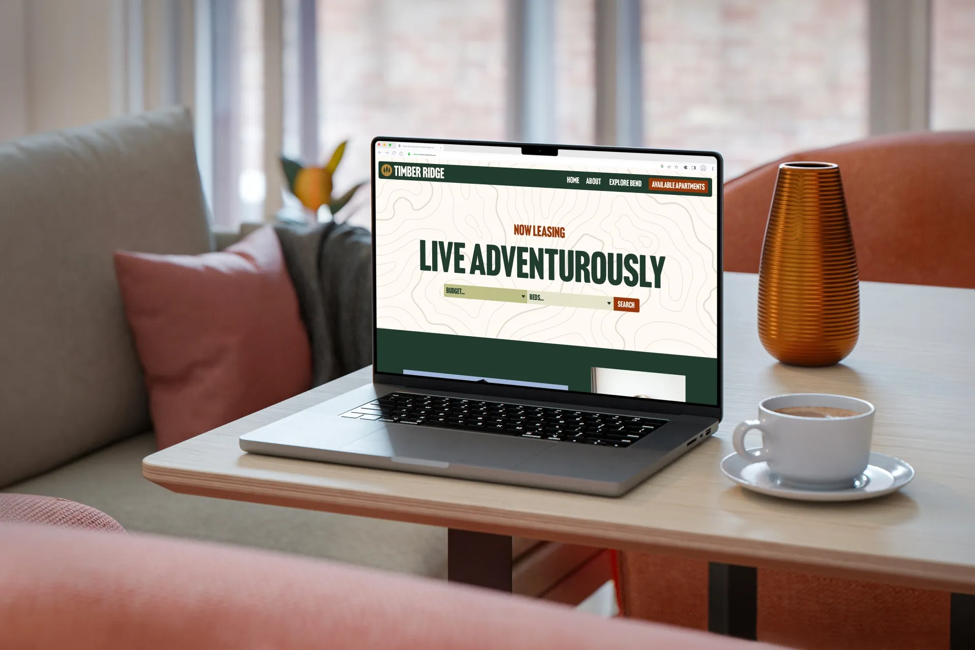 Laptop on table showing Timber Ridge website with text Live Adventurously and search options.