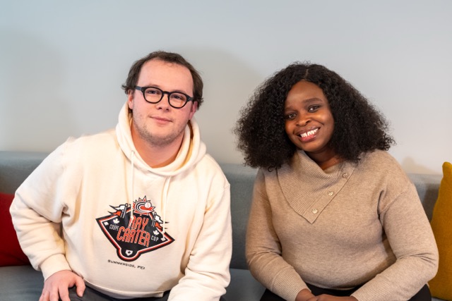 Man in glasses and hoodie and woman with curly hair smiling while sitting on a couch.
