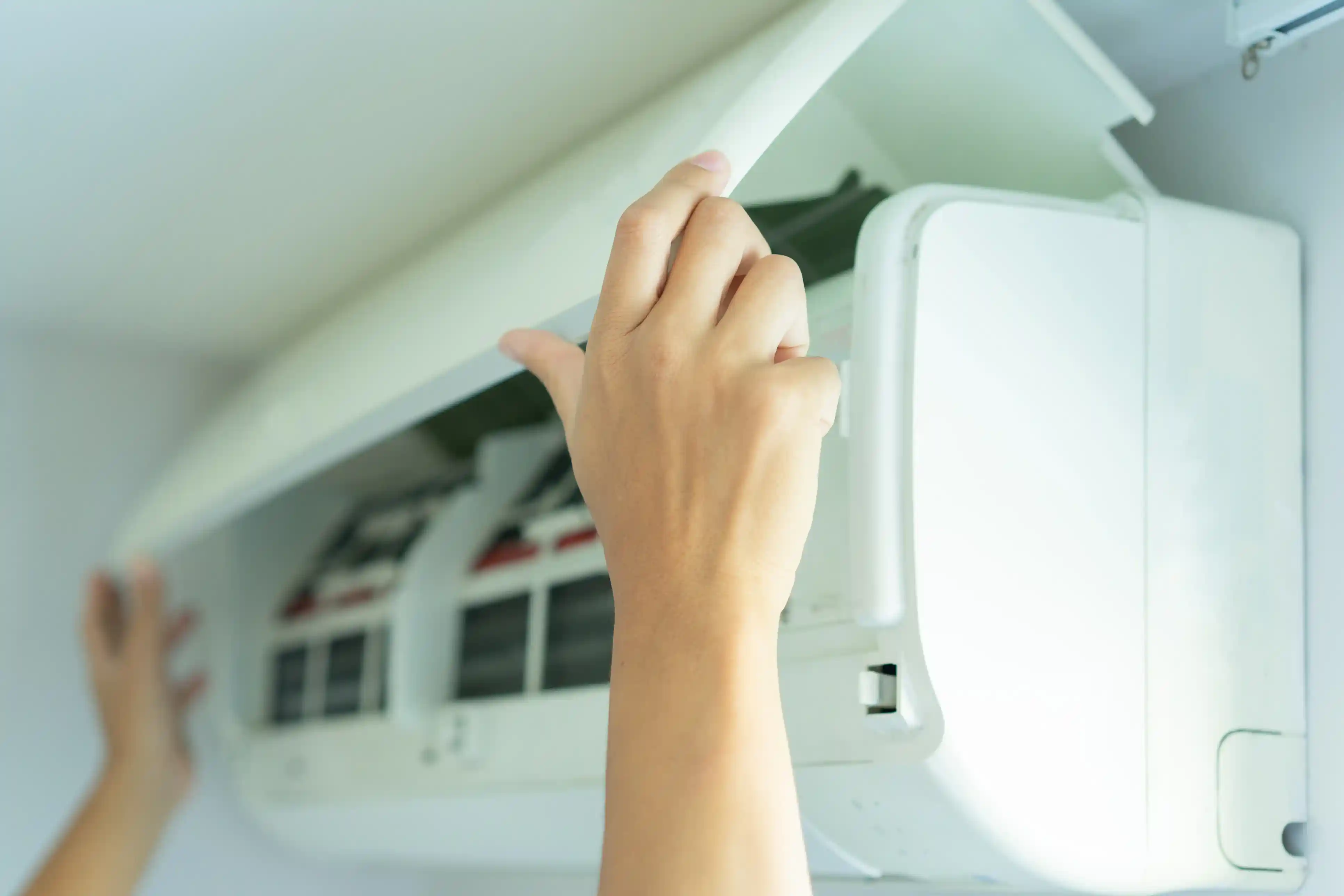 A close-up of a person's hands opening the cover of a wall-mounted air conditioner.