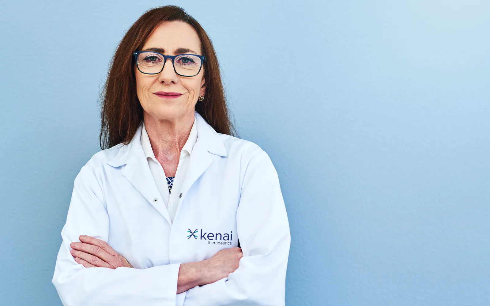 A middle-aged white female scientist wearing a Kenai Therapeutics lab coat.