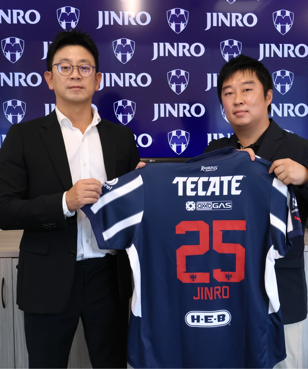 Two men holding a soccer jersey in front of a Jinro backdrop
