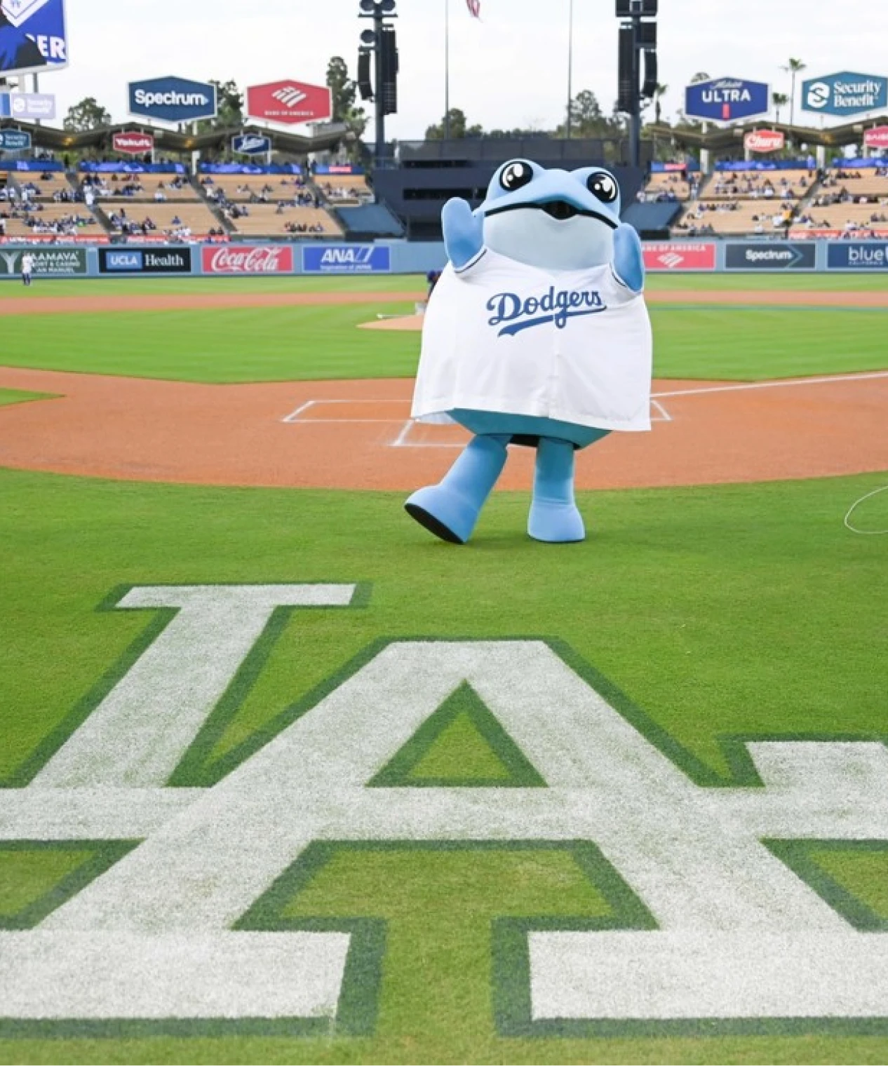 Blue mascot wearing a Dodgers jersey on a baseball field
