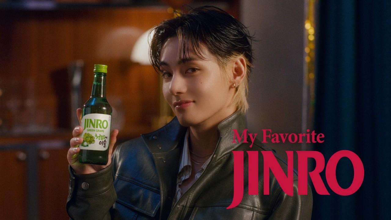V holding a JINRO Green Grape soju bottle in a warmly lit room