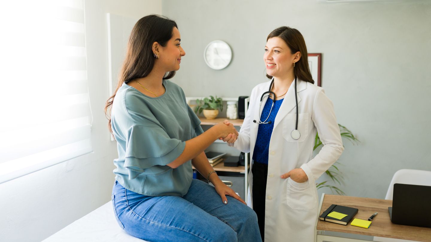Female doctor happily shaking hands with her Hispanic patient after a successful consultation in her office