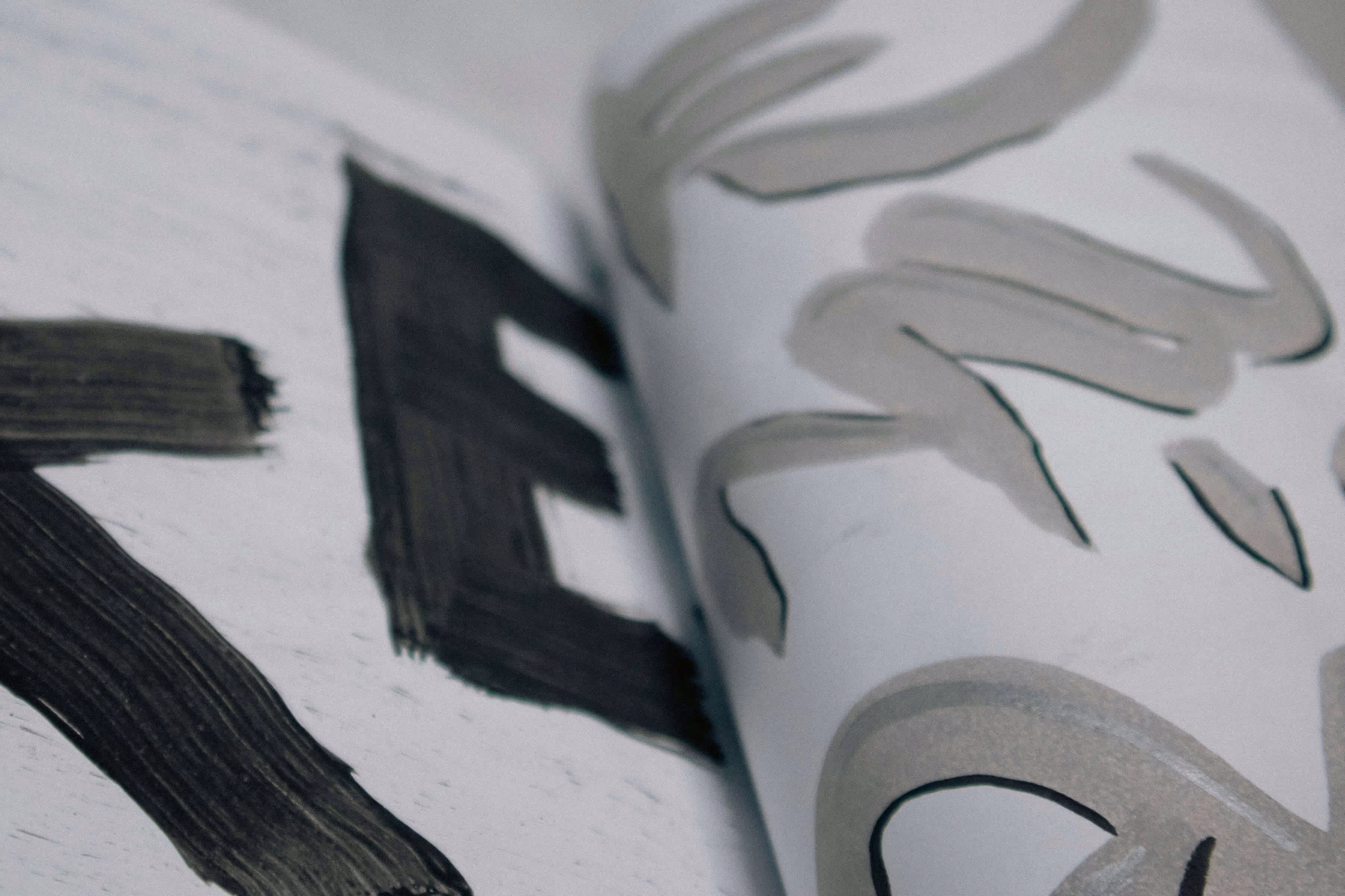 Close-up of an open book showing bold black brushstroke letters and gray abstract brush designs.