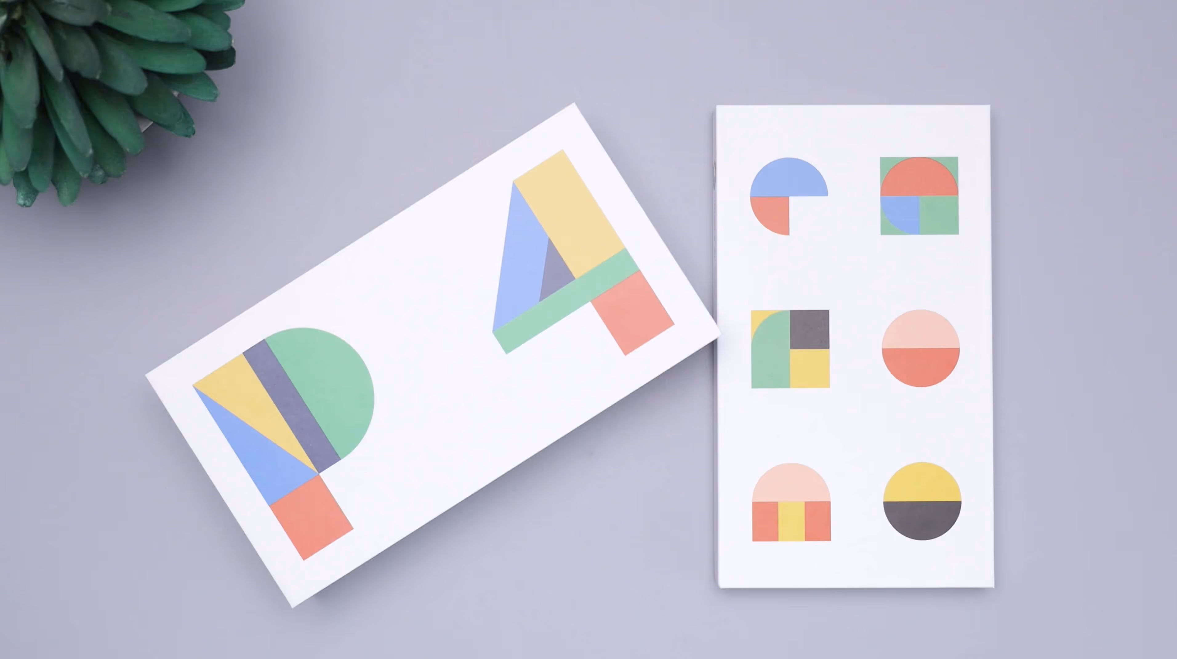 Two white cards on a gray surface with colorful geometric shapes; one card features the letters P and A made from triangles, rectangles, and semicircles, the other card displays six various colorful geometric shapes in a grid.