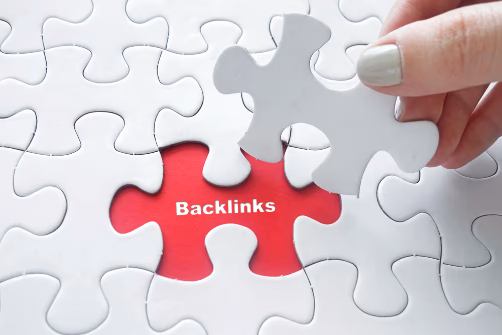 Hand placing a white puzzle piece into a missing spot revealing the word 'Backlinks' on a red background.