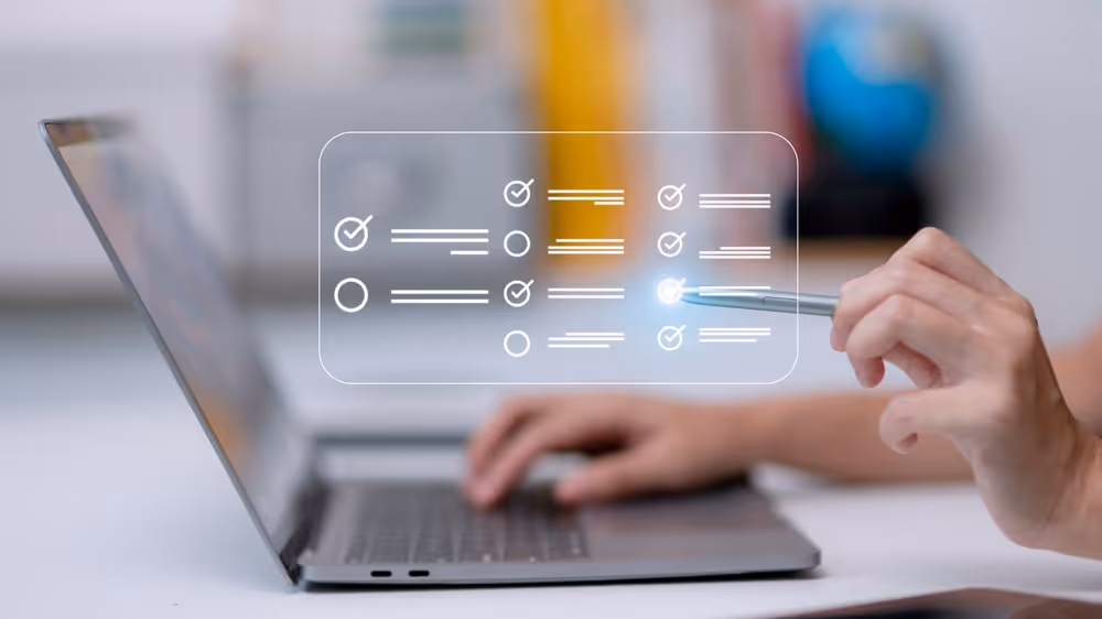 Close-up of hand holding stylus pointing at digital checklist icons floating in front of an open laptop.