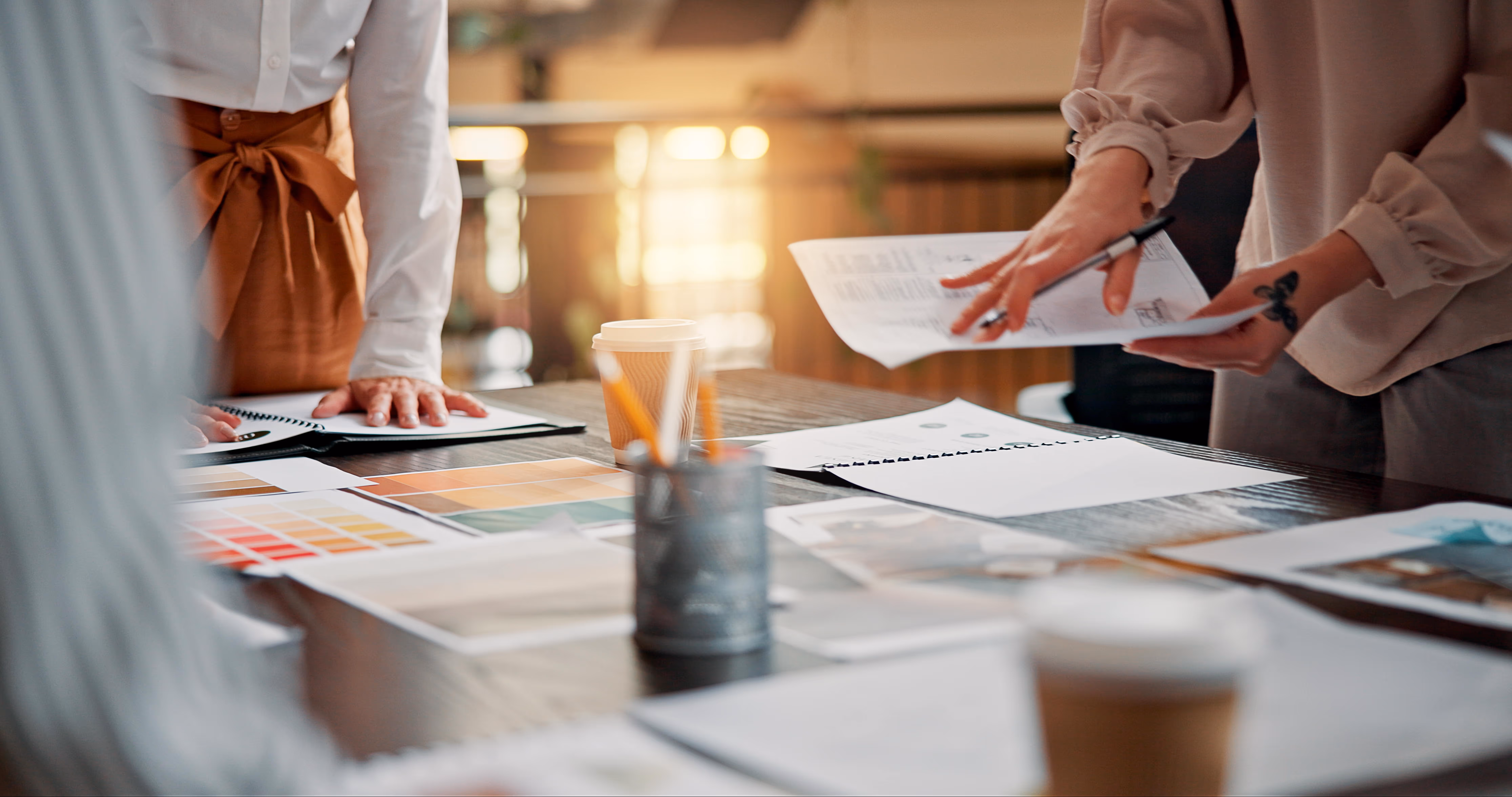 People discussing color swatches and documents on a table with coffee cups in a bright office setting.
