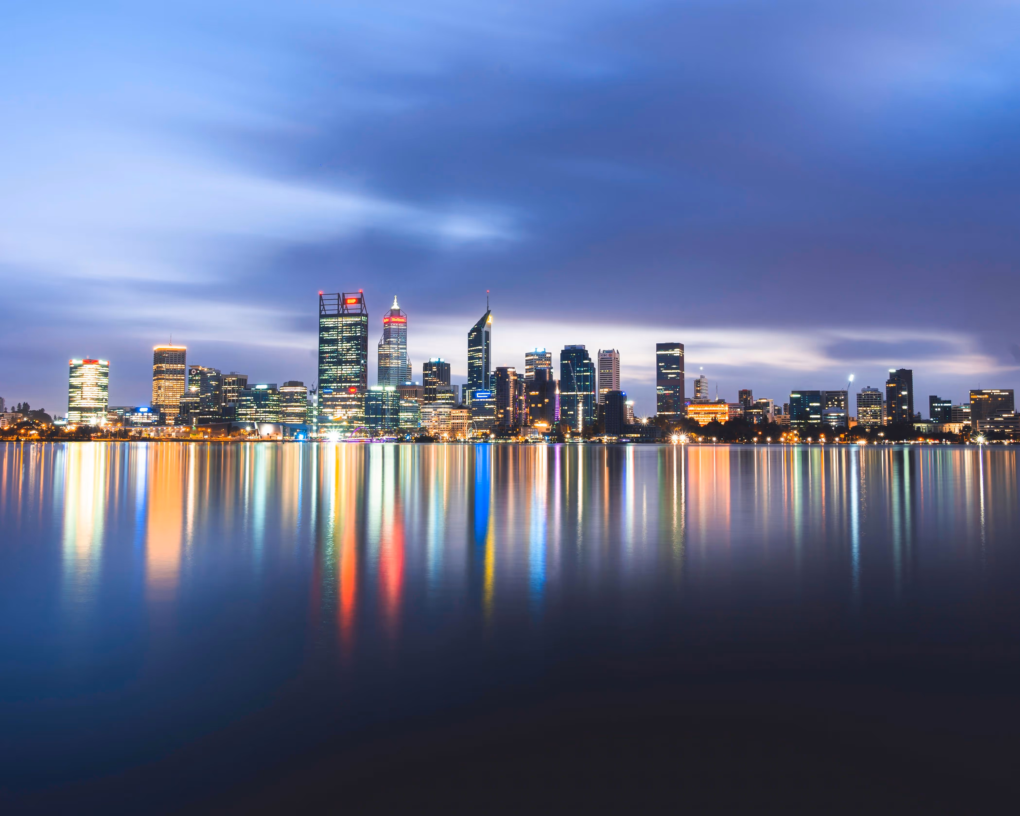 City skyline at dusk with lights reflecting vibrantly on calm water.