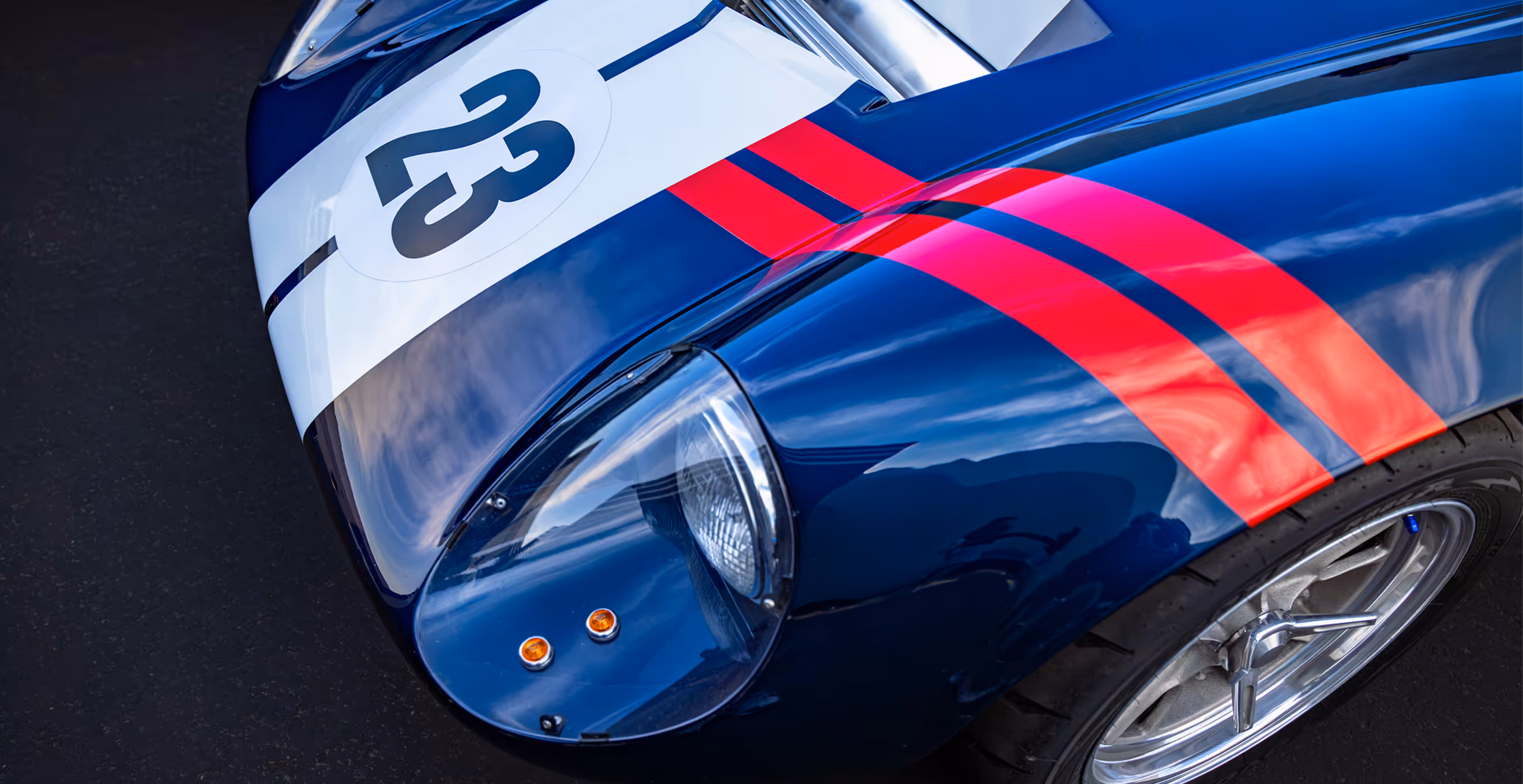 Close-up of front left headlight and blue body with red racing stripes and number 23 on a classic race car.