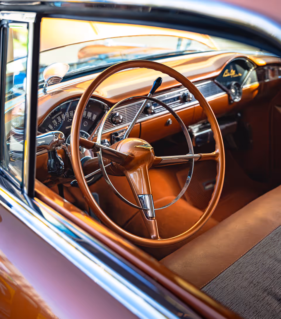 Interior view of a vintage car dashboard and steering wheel in brown tones.