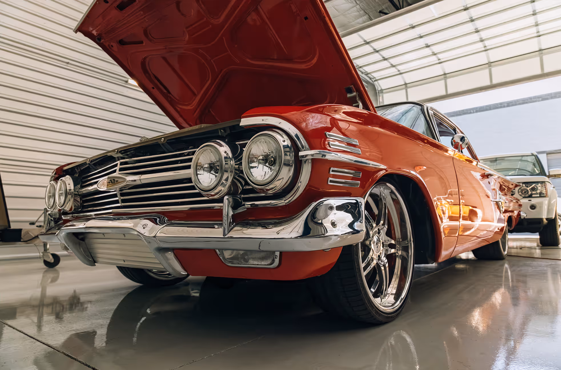 Low-angle view of a shiny red vintage car with its hood open inside a garage.