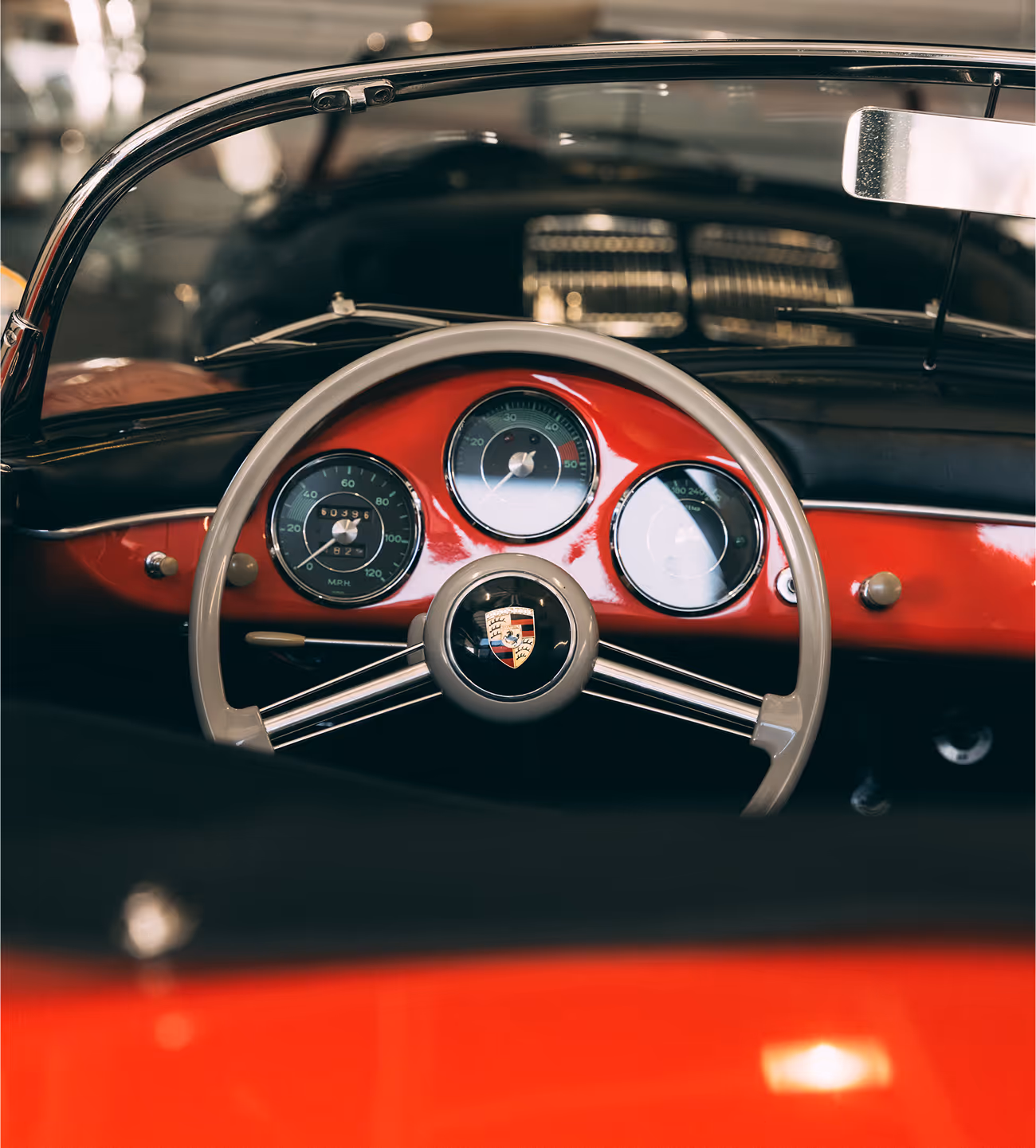Steering wheel and dashboard of a classic Porsche car, featuring round dials and a Porsche emblem in the center.