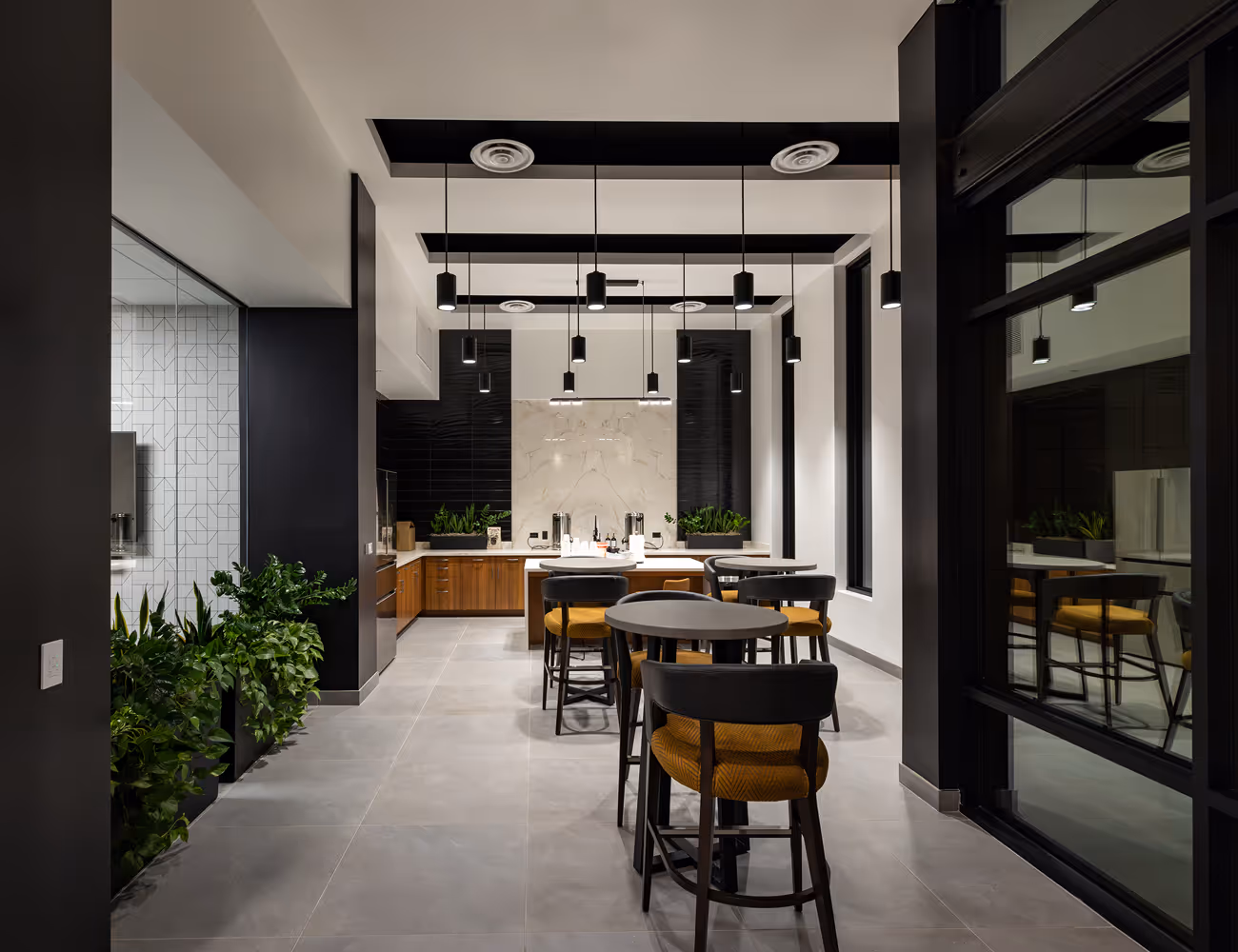 Modern lounge area with pendant lighting, tables, chairs with yellow cushions, and green plants.