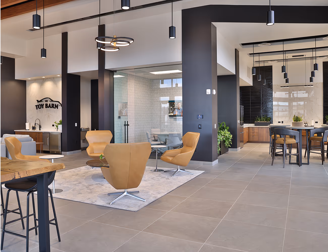 Modern lobby area with tan chairs, tables, and the Toy Barn logo on a marble wall.