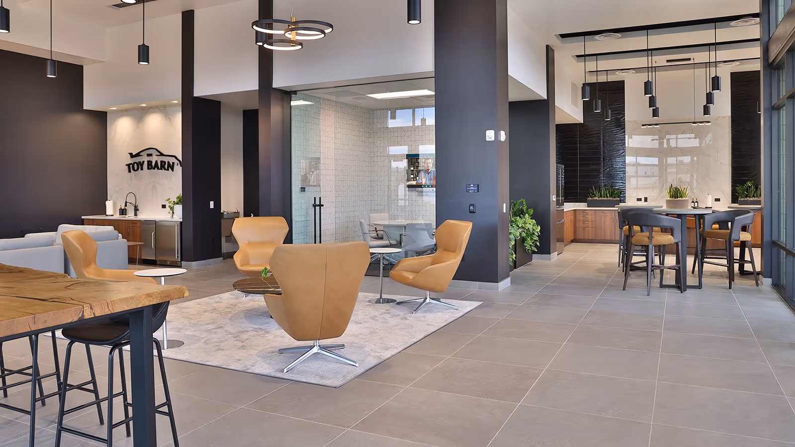 Modern lobby area with tan chairs, tables, and the Toy Barn logo on a marble wall.